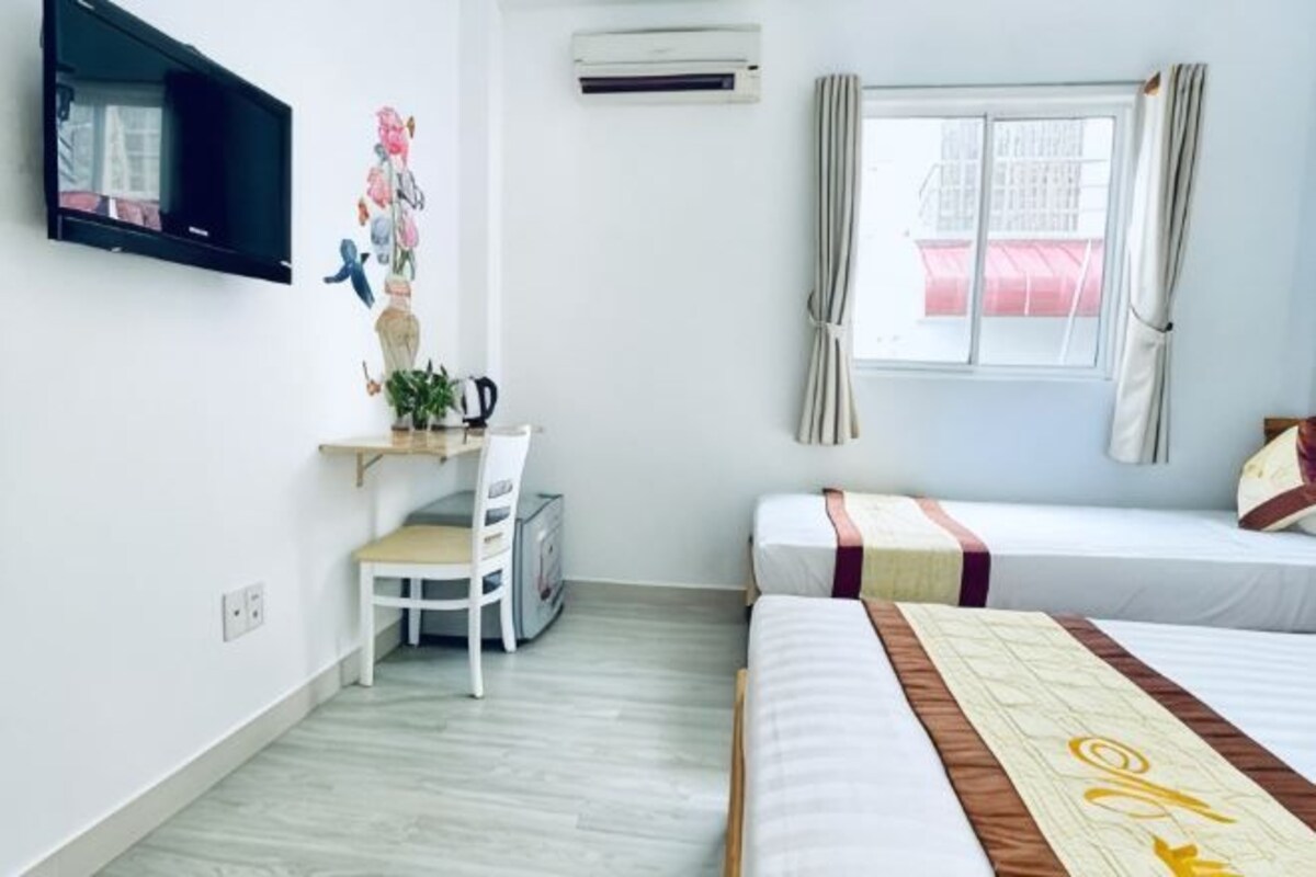 A bedroom with a bed, a desk, a chair, a window with curtains, and an air conditioning unit.