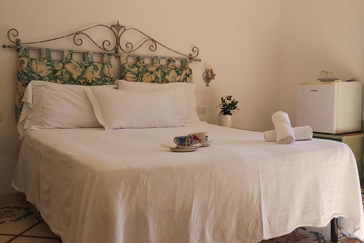 A neatly made bed with a floral-patterned headboard, a small bedside table with a plant, and a white air conditioning unit on the wall.