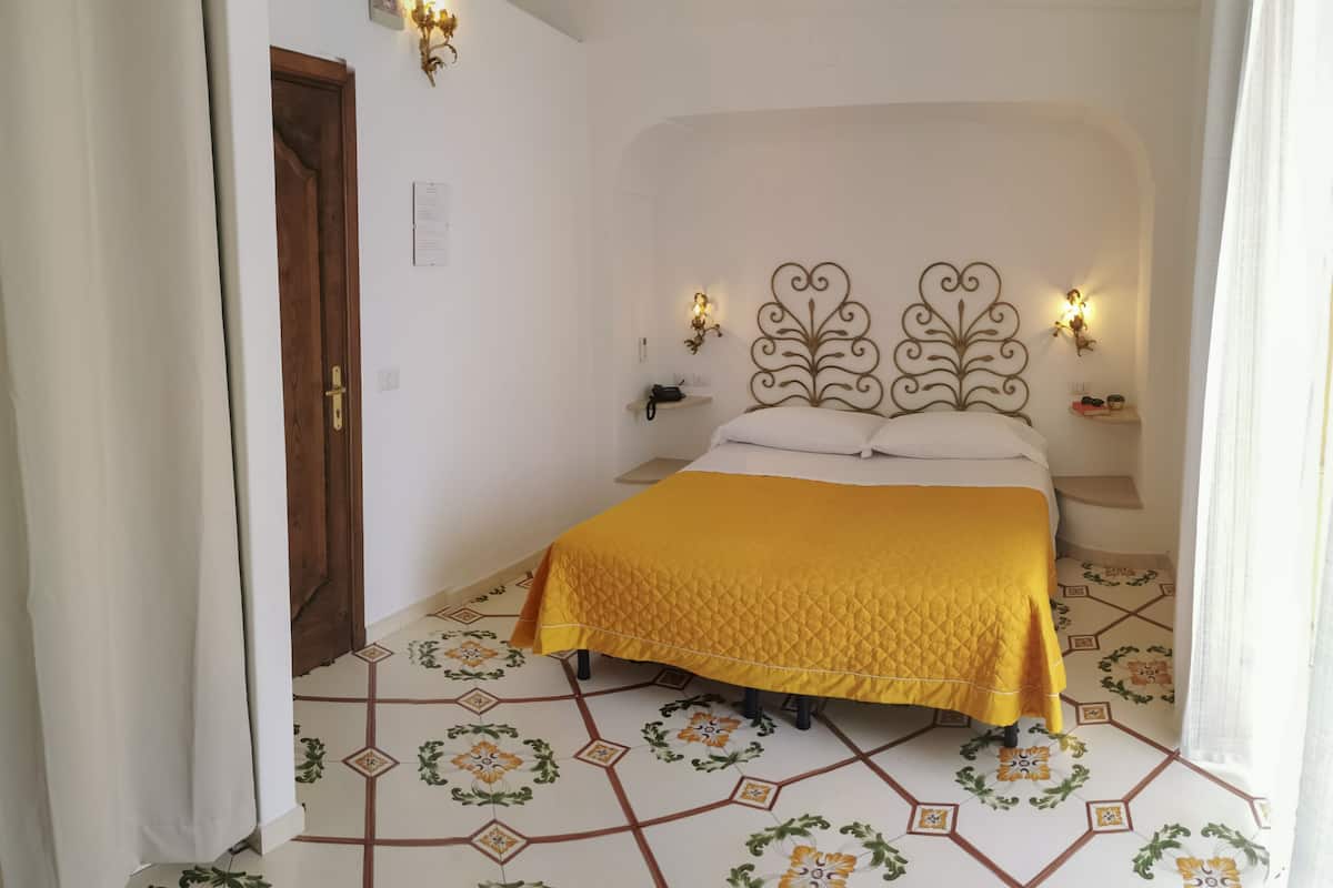 A bedroom with a bed, a nightstand, a wall-mounted shelf, and a decorative headboard.