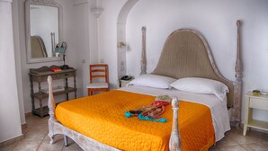 A bedroom with a large bed, a wooden nightstand, a chair, and a desk with a mirror. - Hotel Dimora Fornillo (Positano)