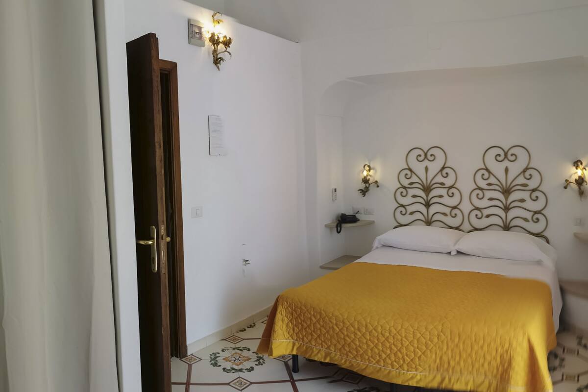 A bedroom with a bed, a nightstand, a wall-mounted lamp, and a door.