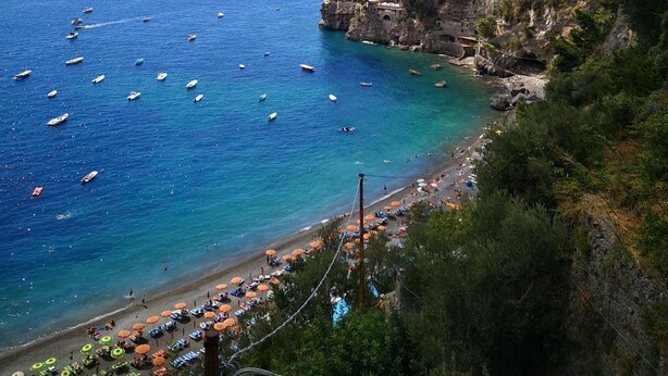A coastal view with boats on the water, a rocky cliff, and a beach with umbrellas. - Hotel Dimora Fornillo (Positano)