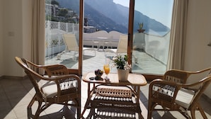 A balcony with wicker chairs and a table, overlooking a mountainous landscape with a view of a coastal village. - Hotel Dimora Fornillo (Positano)