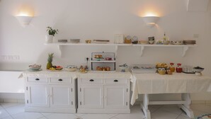 A kitchen with white cabinetry, a countertop with various food items, and two wall-mounted light fixtures. - Hotel Dimora Fornillo (Positano)