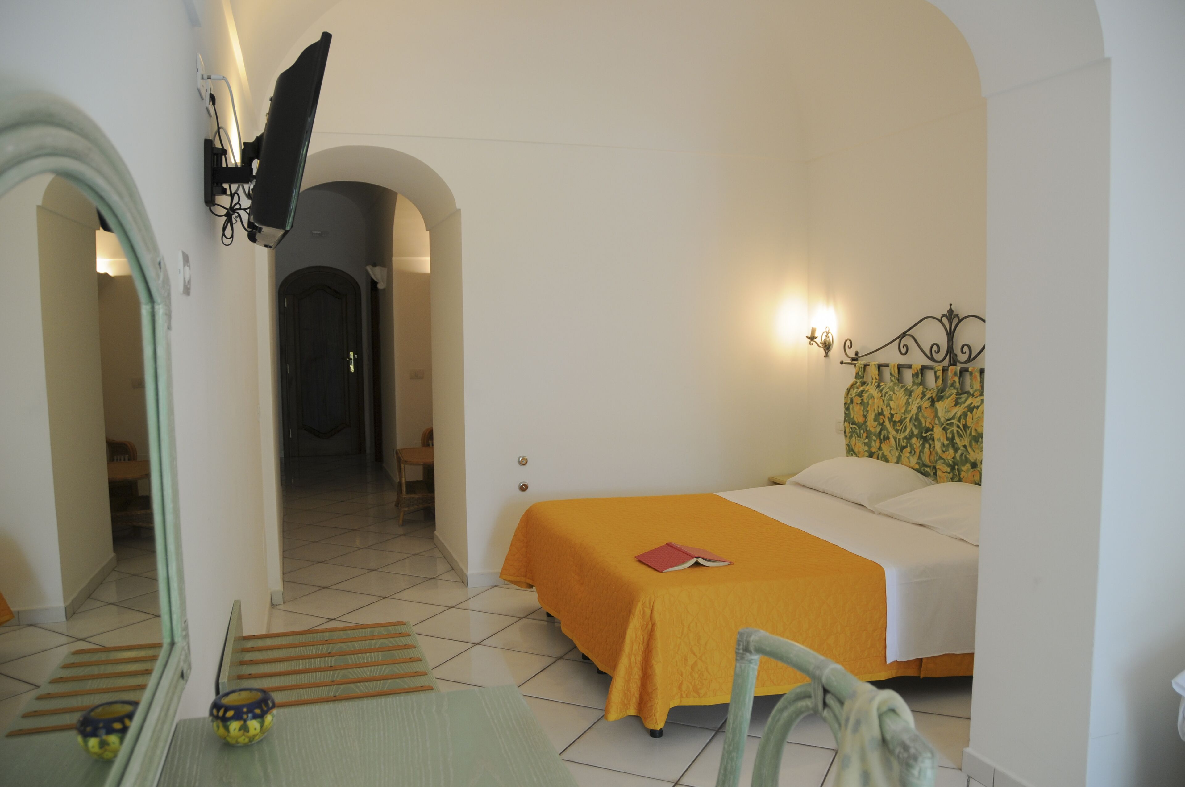 Habitación de hotel con cama, mesita de noche, espejo y puerta que da a otra habitación.