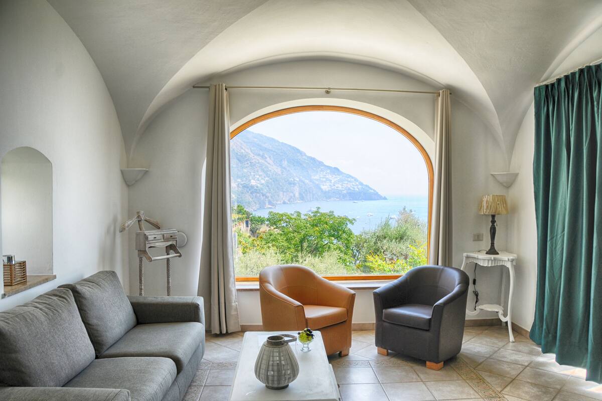 A living room with a view of a mountainous landscape through a large arched window.