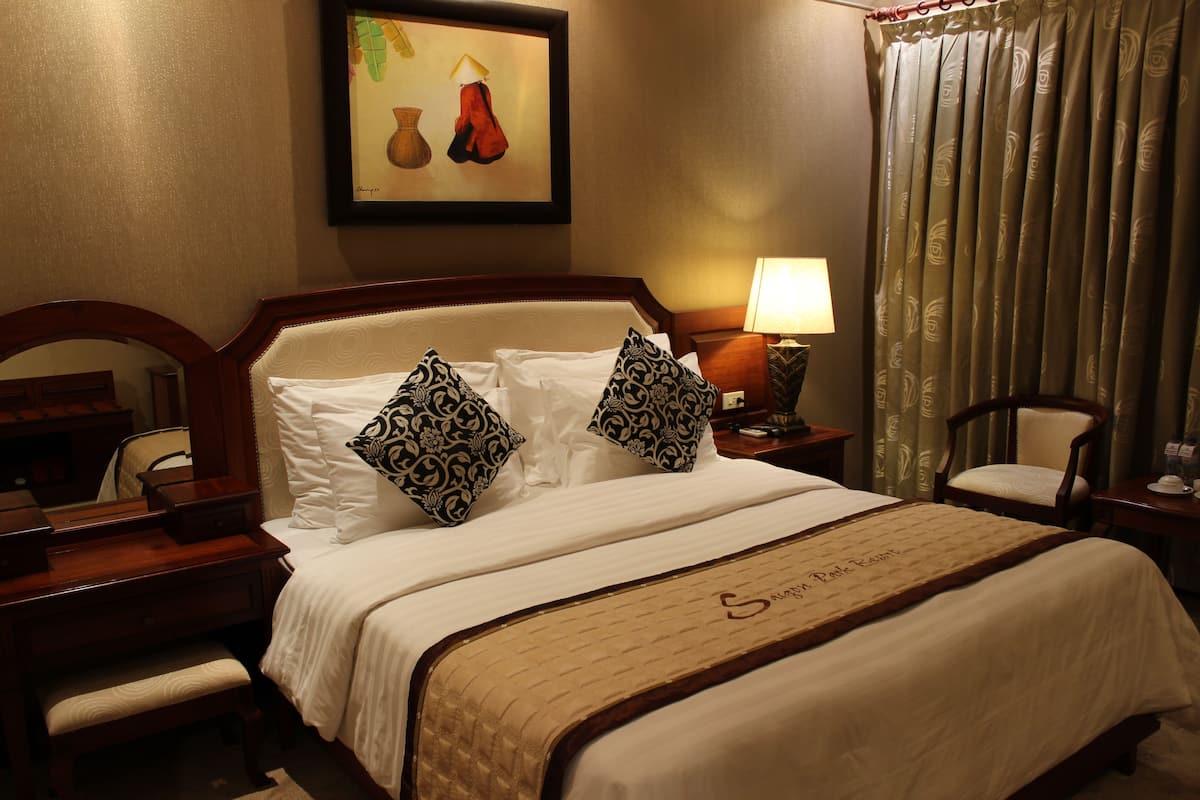 A hotel room with a large bed, a desk, a chair, a lamp, and a painting on the wall.