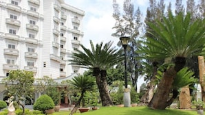 A hotel with a white facade, multiple balconies, and a well-maintained garden with palm trees and a statue. - Saigon Park Resort (Ho Chi Minh City)