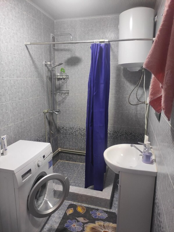 Un baño pequeño con ducha, lavamanos y lavadora.