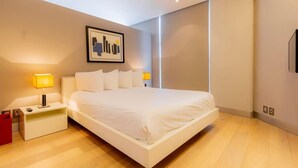 A modern hotel room with a large bed, bedside lamps, a red trash bin, and a framed artwork on the wall.