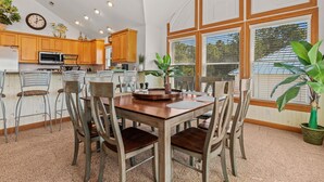 A spacious kitchen with wooden cabinets, a dining table with chairs, and a large window providing natural light. - Inn-Seaclusion: Elevator, Private Pool & Hot Tub, Theater Room (Corolla)