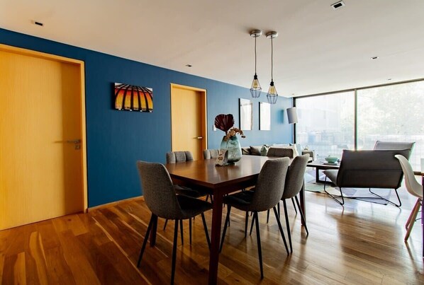 Ein moderner Essbereich mit Holztisch und -stühlen, einer blauen Akzentwand und einem großen Fenster mit Blick auf die Stadt.