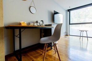 Ein modernes Zimmer mit Schreibtisch aus Holz, einem weißen Stuhl, einem Fernseher und einem großen Fenster.