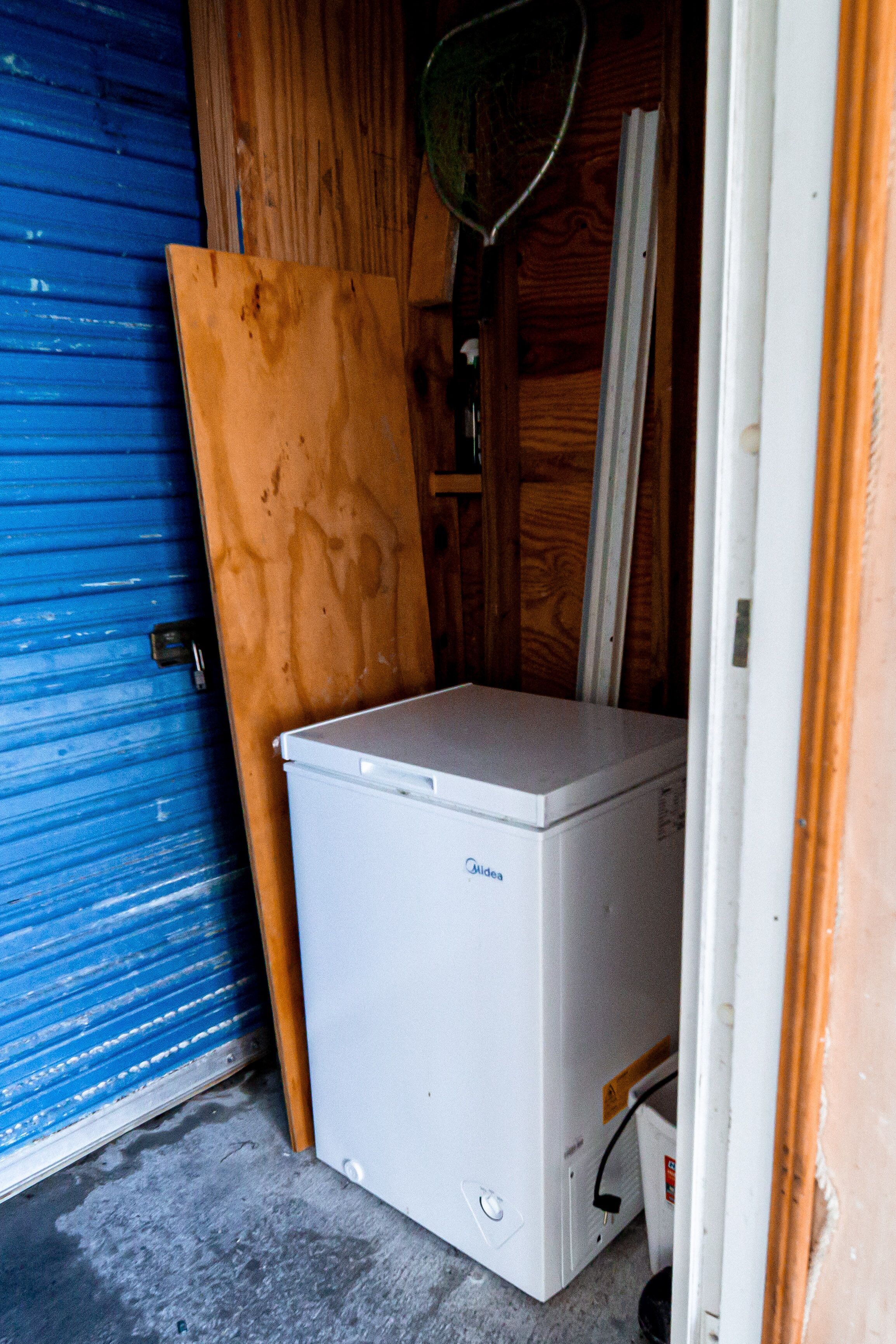 Un petit réfrigérateur blanc, installé dans un espace réduit et fermé, avec une porte bleue et des murs en bois.