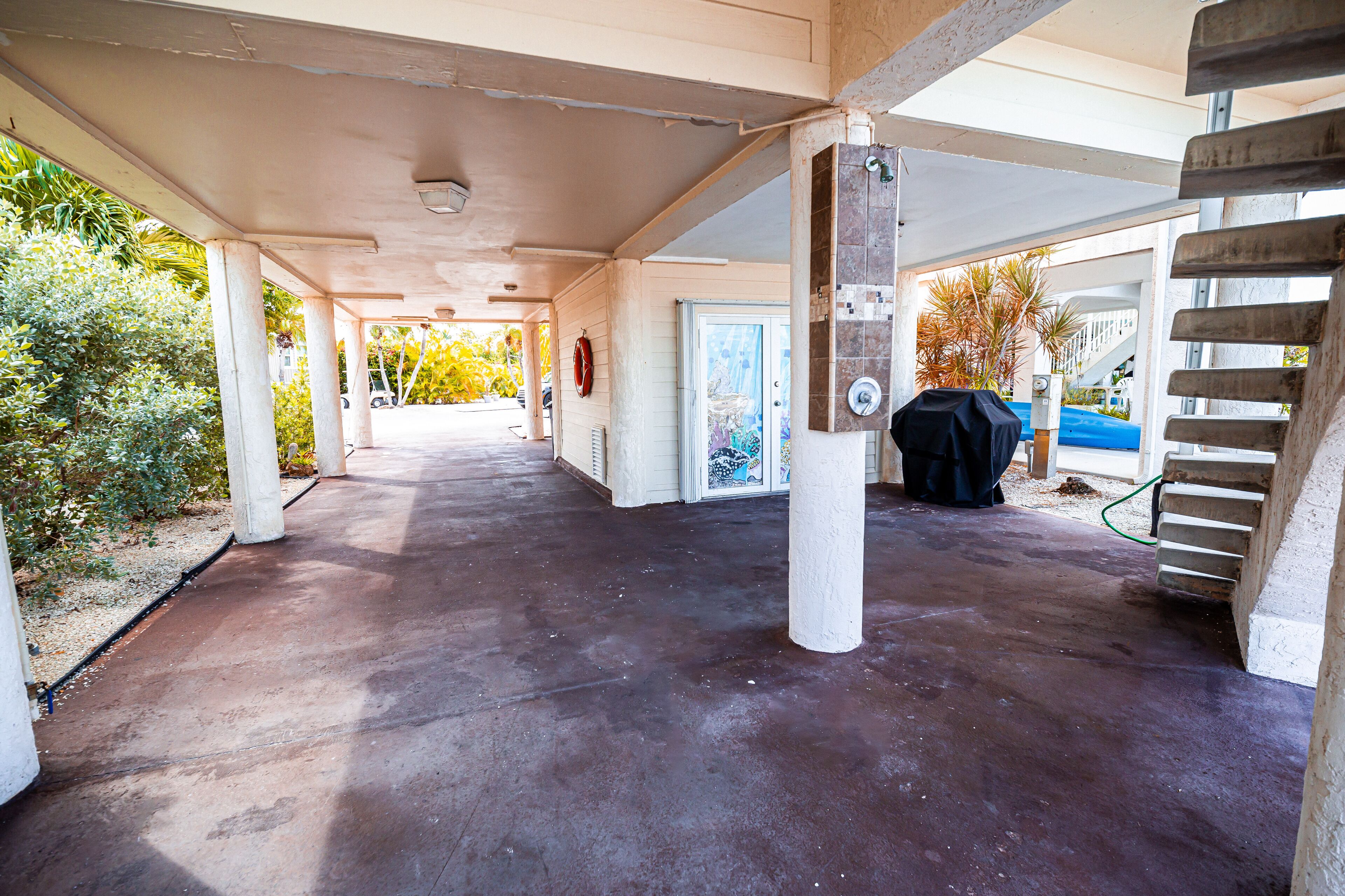 A covered outdoor area with concrete flooring, columns, and a staircase.