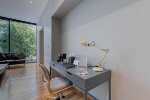 Un espace de bureau moderne comprenant un bureau, une chaise, une lampe et une vue sur les arbres à travers de grandes fenêtres.