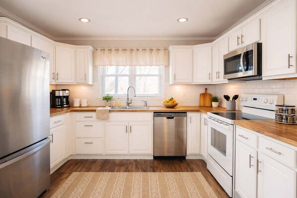 A modern kitchen with white cabinetry, stainless steel appliances, a wooden countertop, and a built-in dishwasher.
