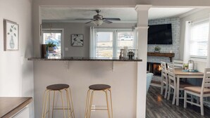 Une cuisine avec un coin bar, deux tabourets, un ventilateur de plafond et une cheminée.