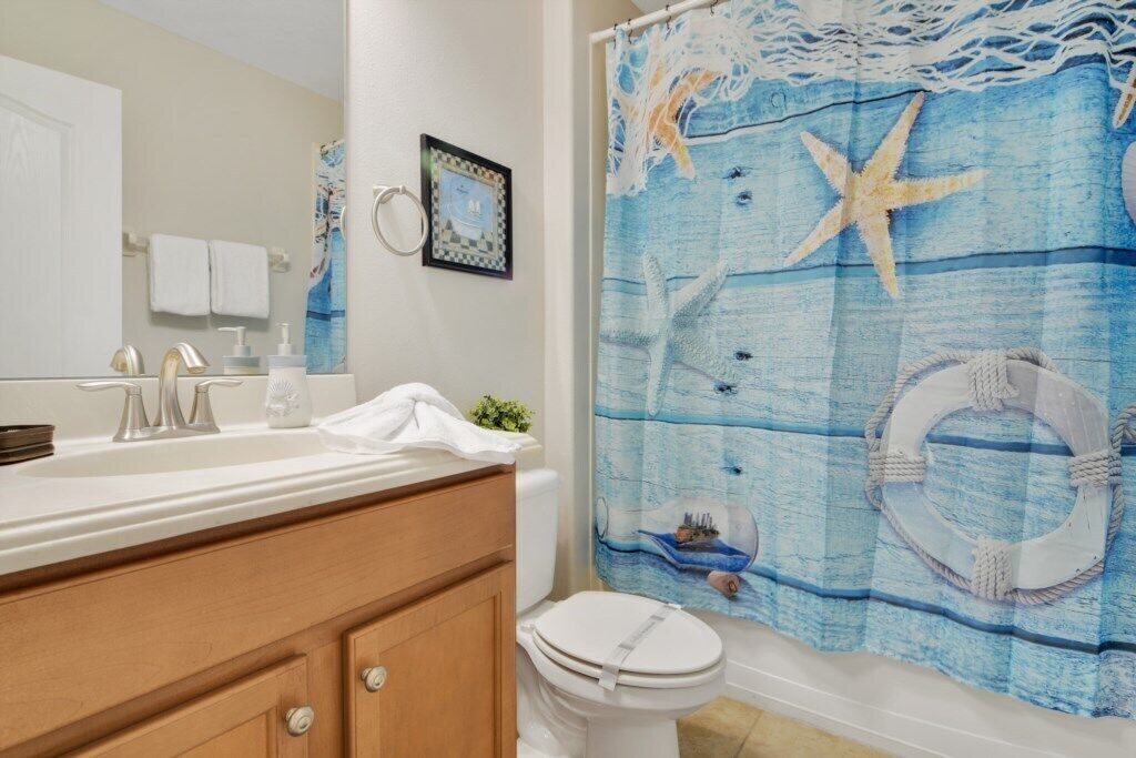 A bathroom with a white sink, a toilet, and a shower curtain with a nautical theme.
