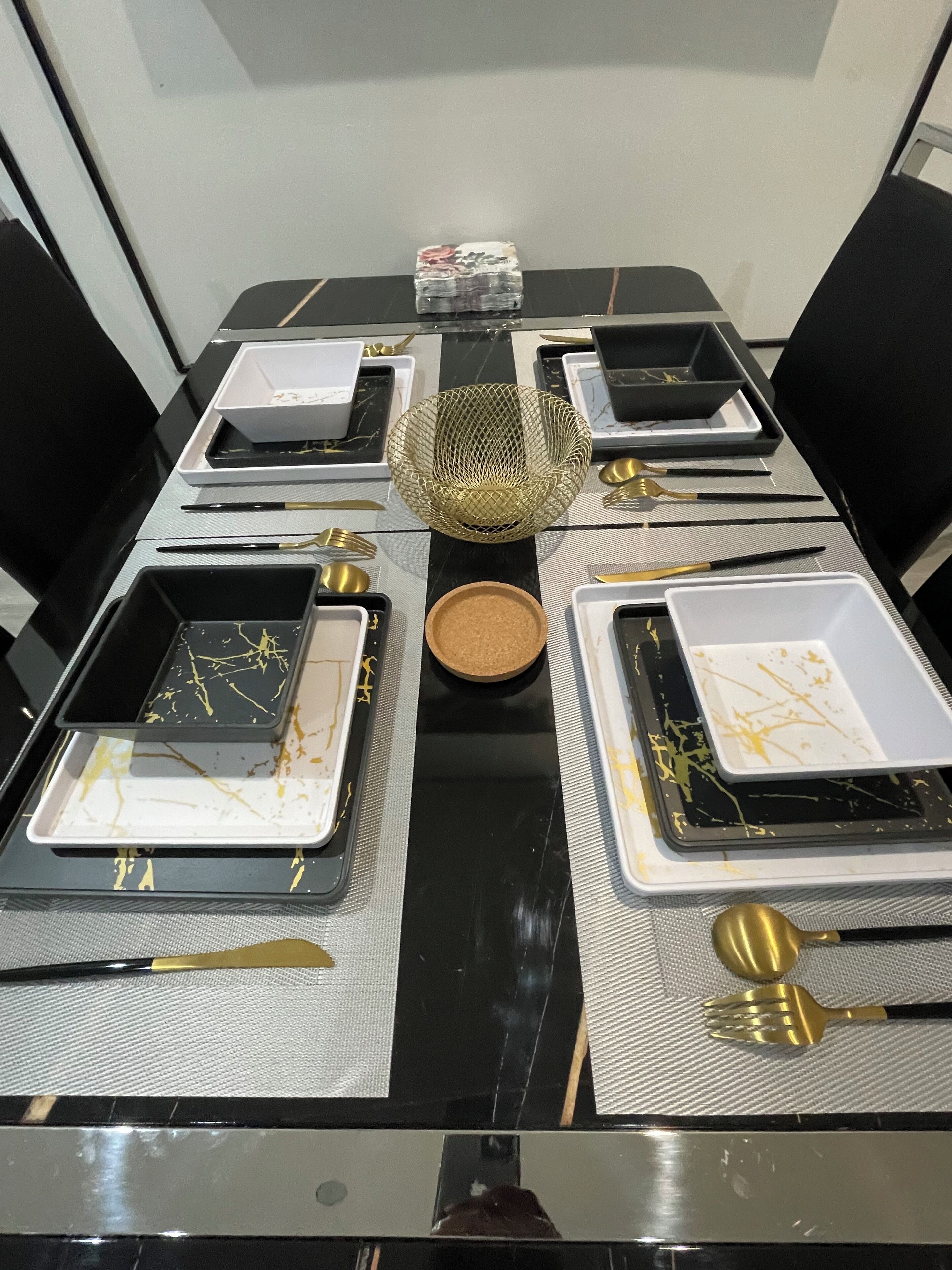 Una mesa de comedor con platos blancos y negros, cubiertos dorados y un centro de mesa decorativo.