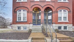 A red brick building with three large arched doors and a stone staircase leading to the entrance.