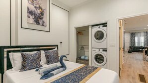 A hotel room with a bed, a washing machine, and a bathroom visible through an open door.