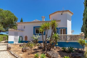 A two-story building with a blue and white facade, a small garden with cacti and succulents, and a clear blue sky.