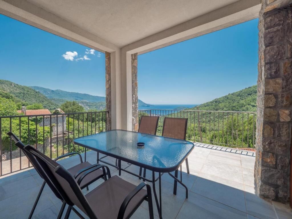 Un balcón con mesa y sillas de vidrio, con vistas a un paisaje montañoso.