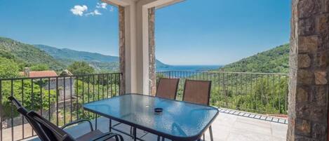 Un balcón con mesa y sillas de vidrio, con vistas a un paisaje montañoso.