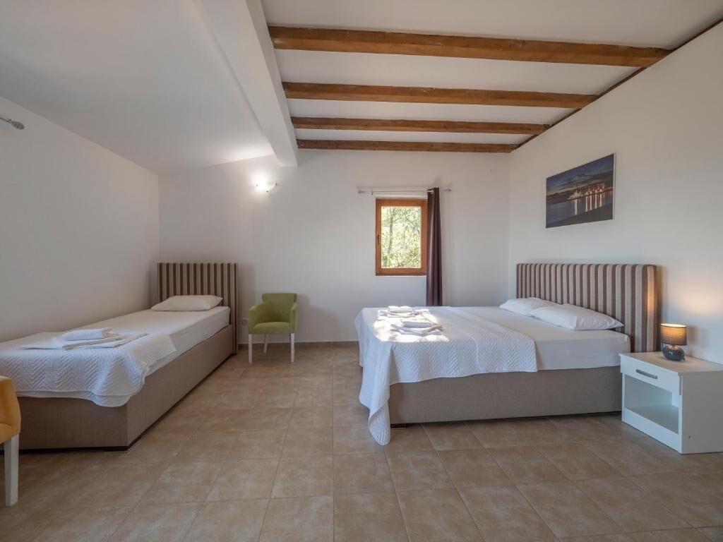 A bedroom with two single beds, a window, a chair, and a nightstand with a lamp.