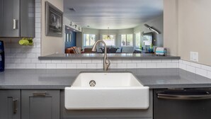 A modern kitchen with a large sink, grey cabinets, and a dining area visible through the window. - Riviera Gardens Minutes from Downtown (Palm Springs)