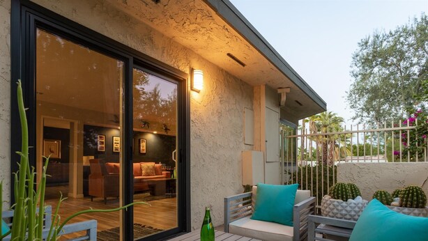 An outdoor patio area with a wooden table, a sofa with teal cushions, and a cactus plant. - Riviera Gardens Minutes from Downtown (Palm Springs)