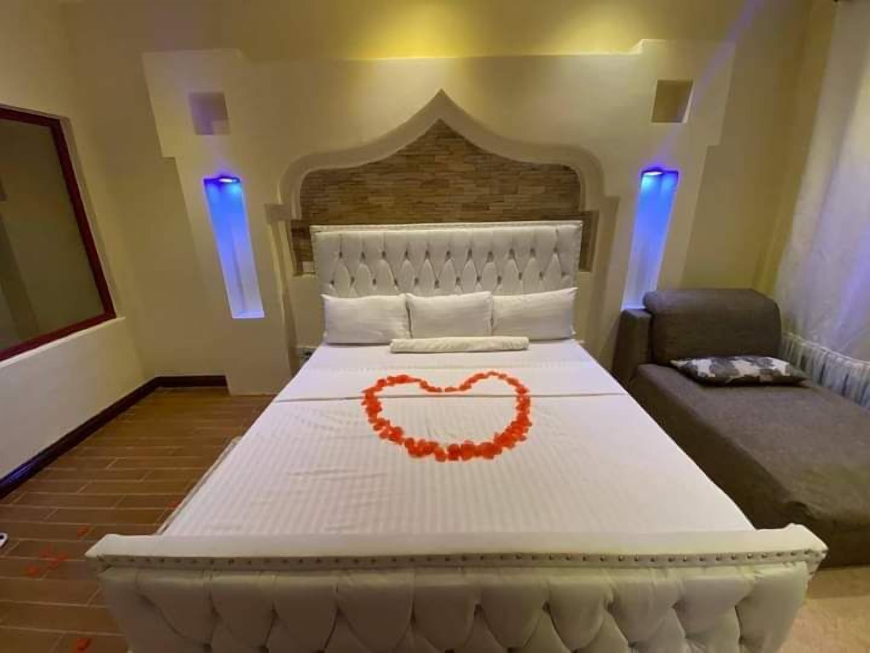 A hotel room with a large bed, a tufted headboard, and a heart-shaped decoration on the bed.