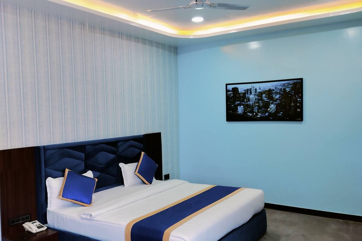 A modern hotel room with a large bed, a nightstand, a glass coffee table, and a cityscape view.