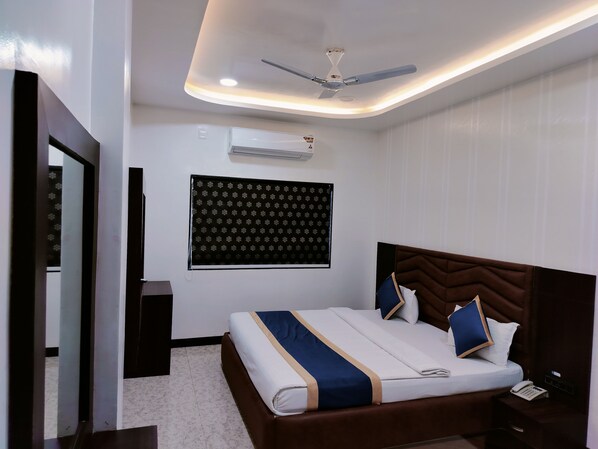 A modern bedroom with a bed, a ceiling fan, an air conditioning unit, and a patterned wall hanging.
