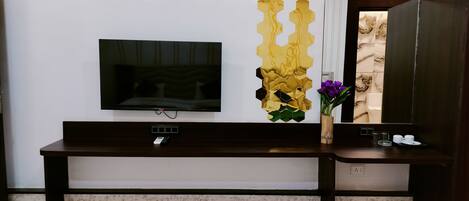 Quarto de hotel moderno com televisão de tela plana na parede, mesa de console de madeira com um vaso de flores e um espelho grande refletindo a decoração do quarto.