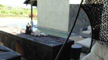 A wooden deck with a white cushioned chair, a stone bench, and a small table.