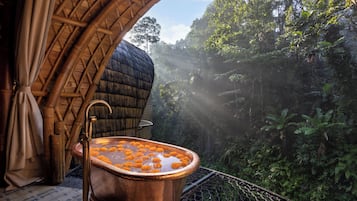 Uma banheira de cobre cheia de água e flores de calêndula, com uma exuberante floresta ao fundo.