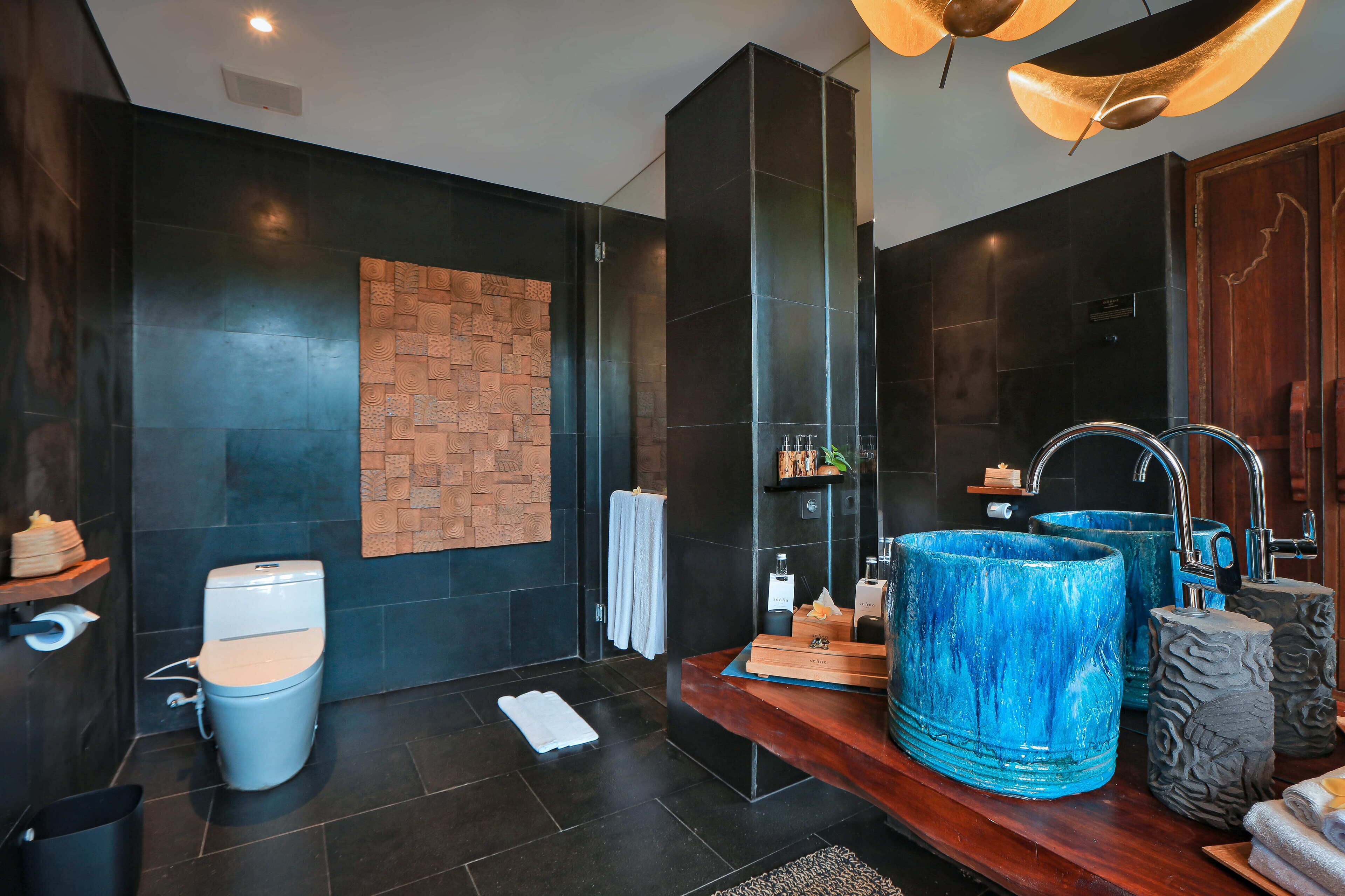 A modern bathroom with dark tiles, a wooden vanity, and two large blue sinks.