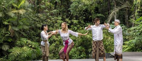 A group of people performing a dance on a wooden platform surrounded by lush greenery.
