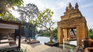 A serene pool area with lounge chairs, a wooden deck, and a traditional architectural structure.