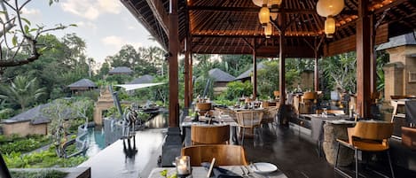 A restaurant with outdoor seating overlooking a pool and lush greenery.