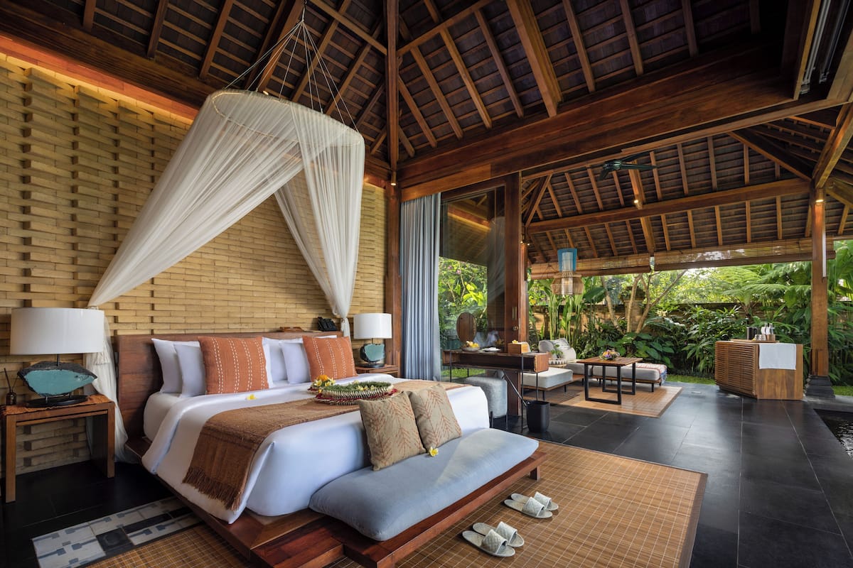 A spacious bedroom with a large bed, bedside tables, a desk, and a view of lush greenery.