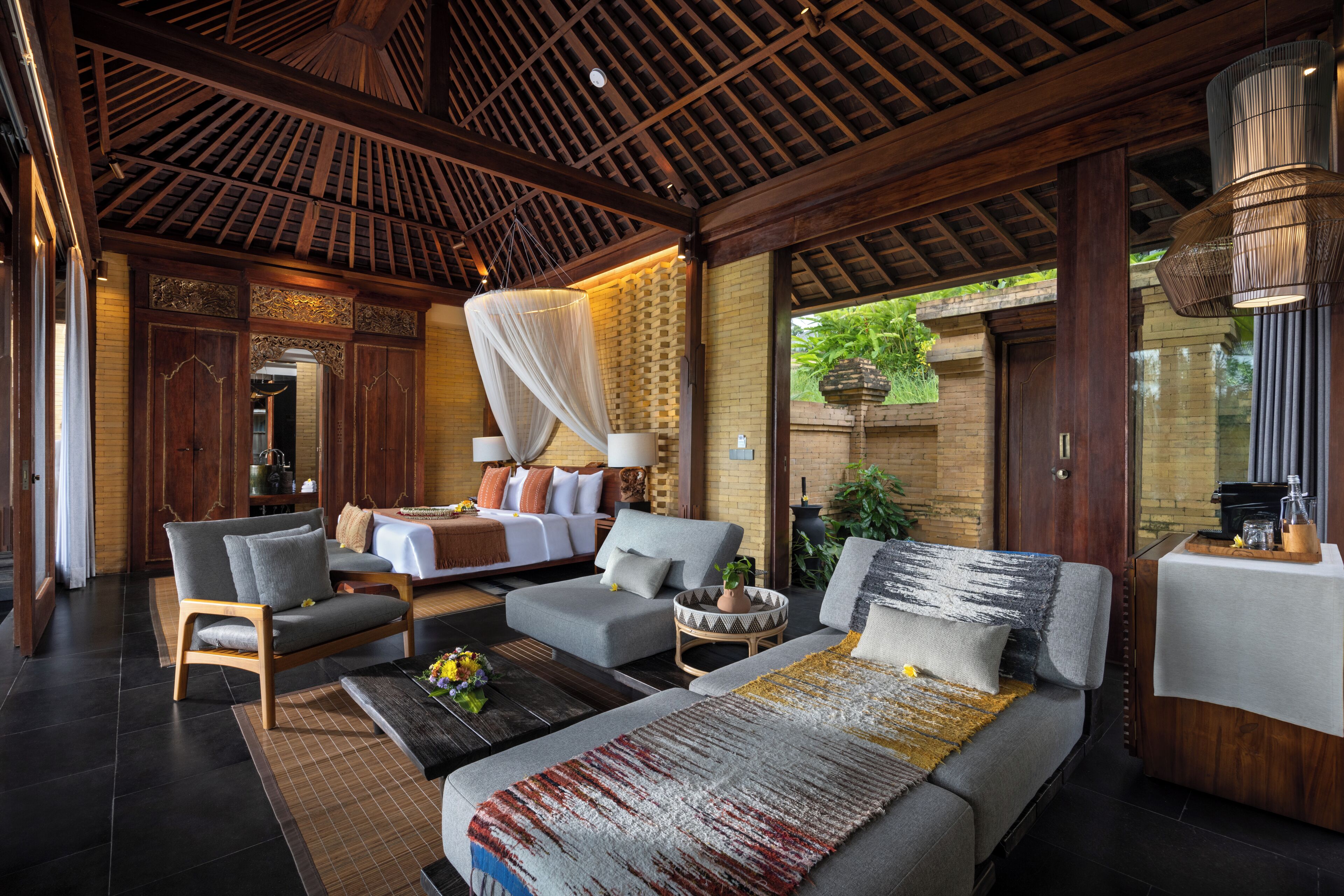 A spacious room with a large bed, two sofas, and a coffee table. There is a wooden ceiling and a large window.