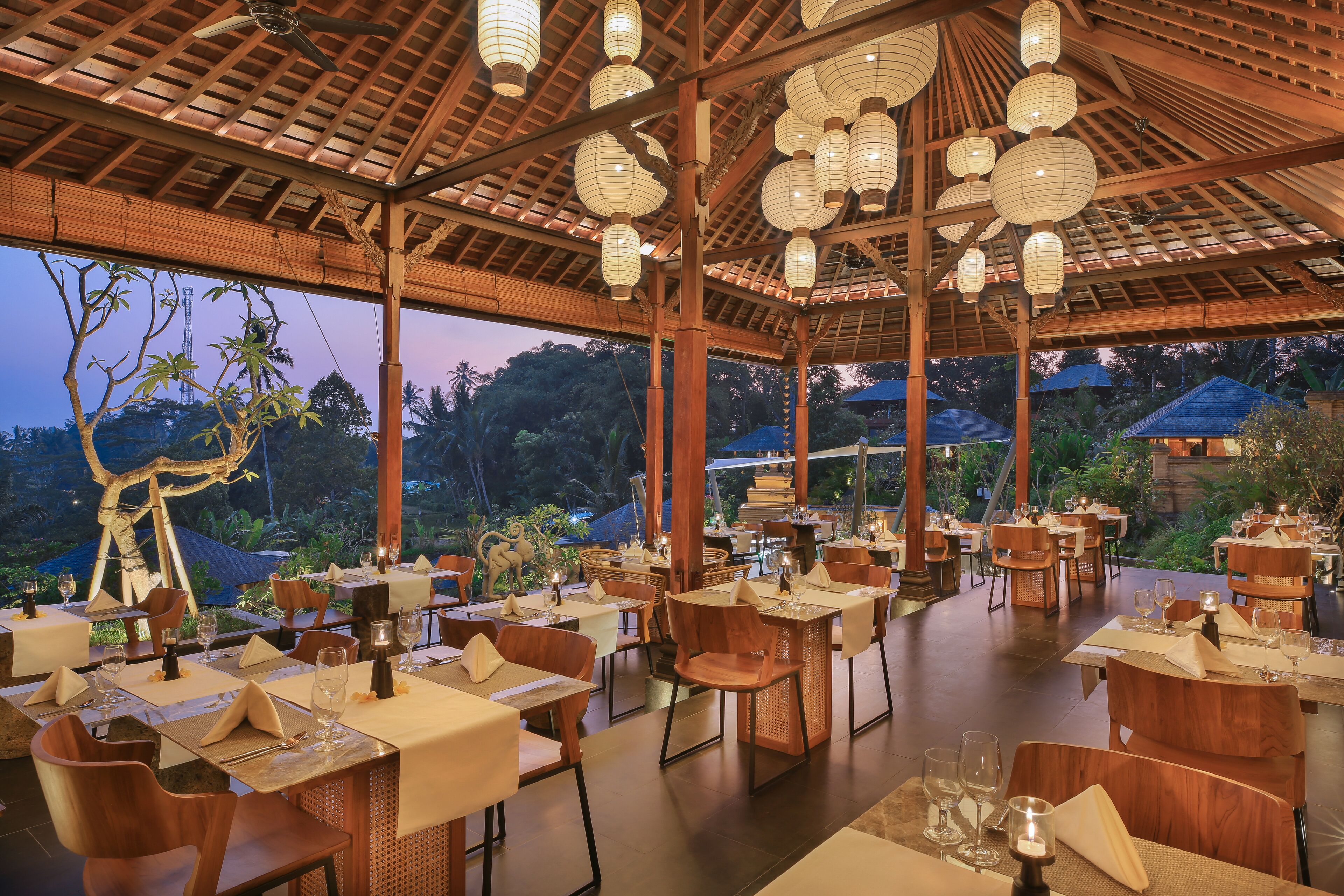 An outdoor dining area with wooden tables and chairs, surrounded by a wooden pergola with hanging lanterns.