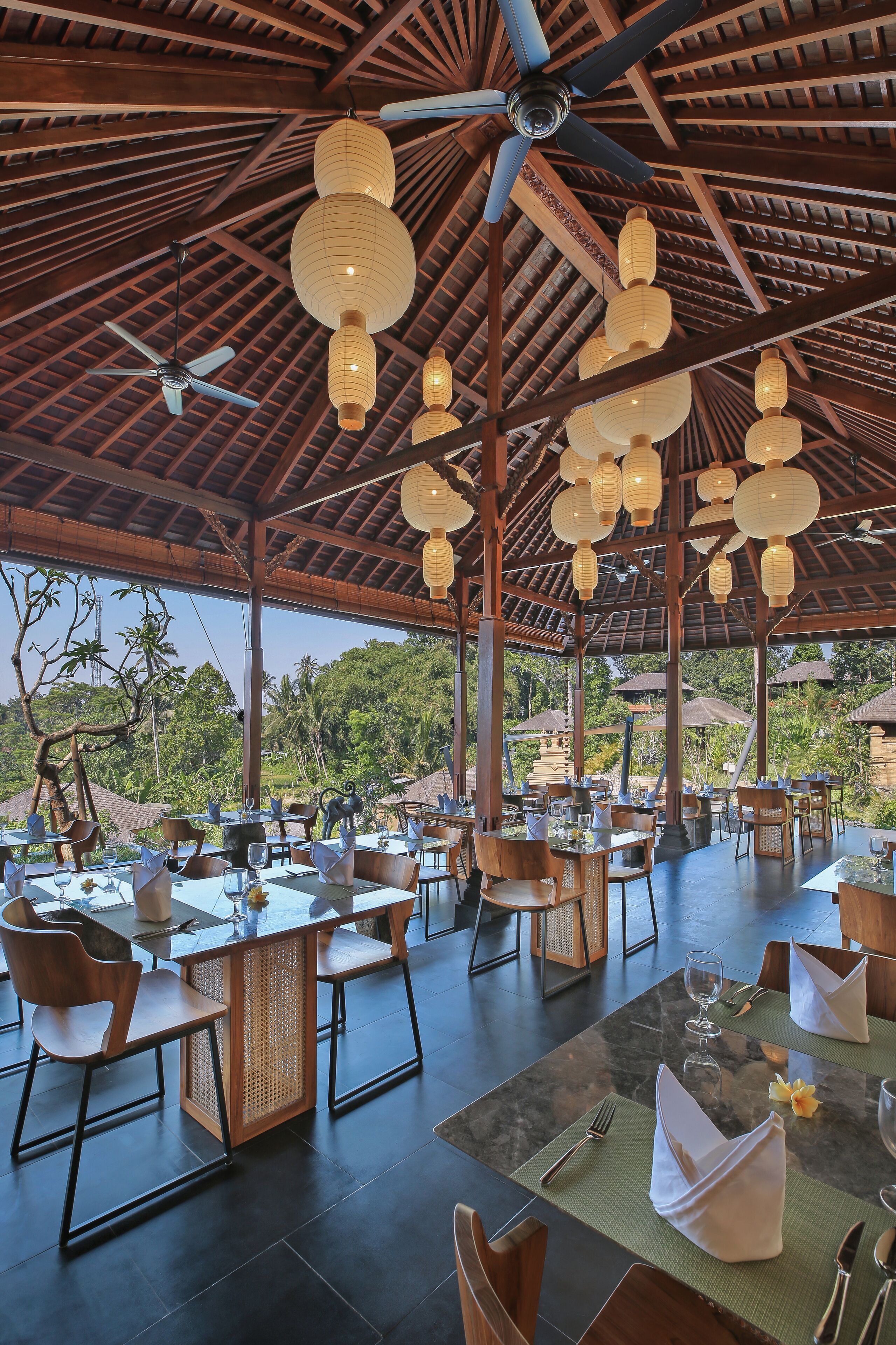 A restaurant with tables set for dining, ceiling fans, and hanging lanterns.