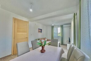 A modern room with a dining table, chairs, a wooden door, a painting on the wall, and a view of another room through a window. - Talia Apartments (Lastva Grbaljska)