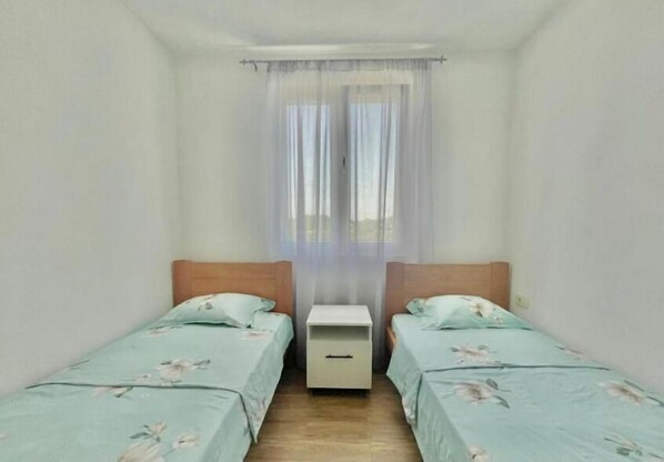 A small, clean room with two single beds, a nightstand, and a window with sheer curtains. - Talia Apartments (Lastva Grbaljska)