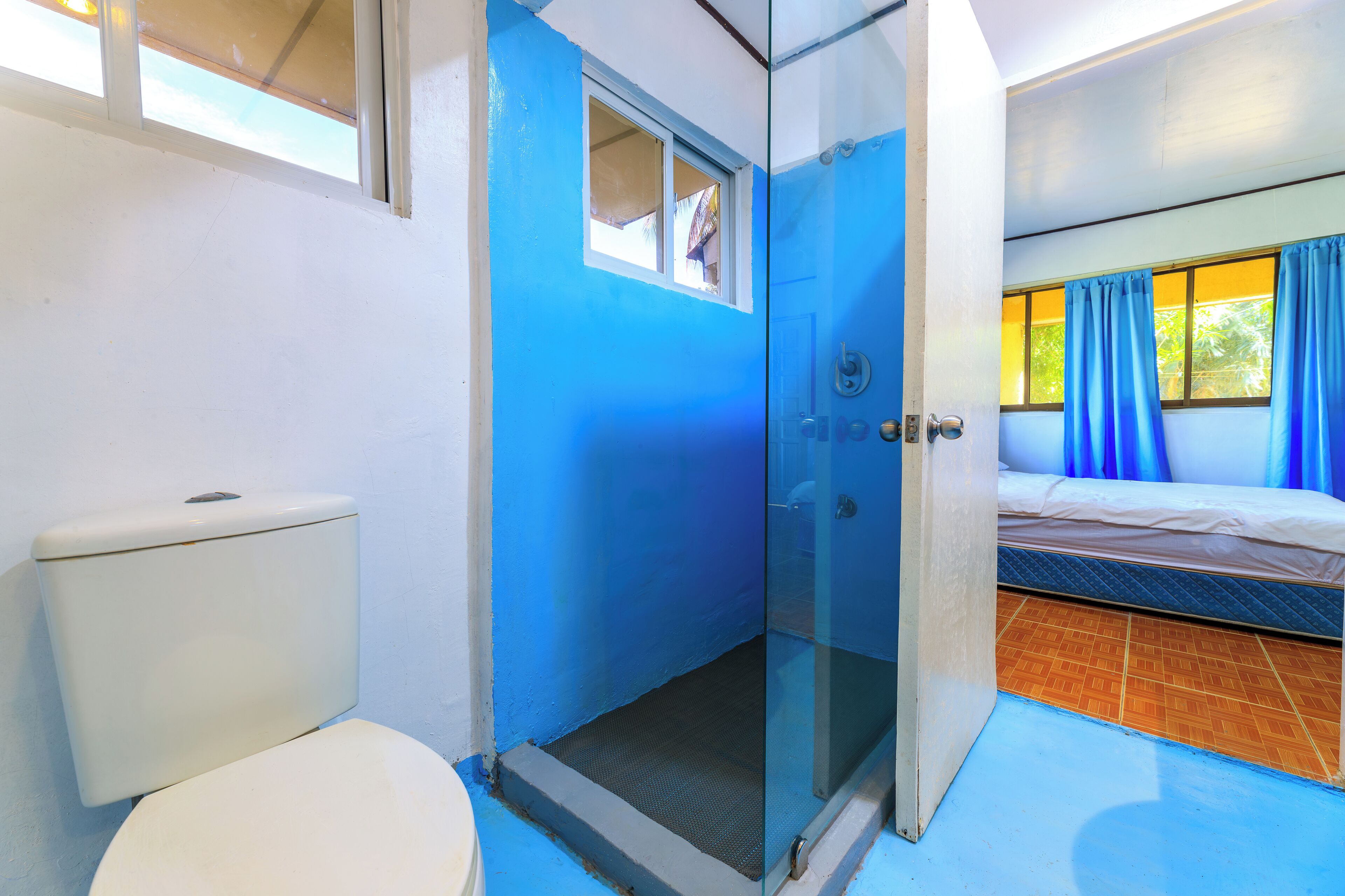 A bathroom with a toilet, a glass-enclosed shower, and a bed with blue curtains.