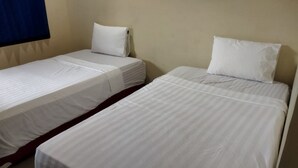 Two single beds with white linens in a room with plain walls and a blue curtain. - Homestay Tentrem Simpang Lima (Pati)